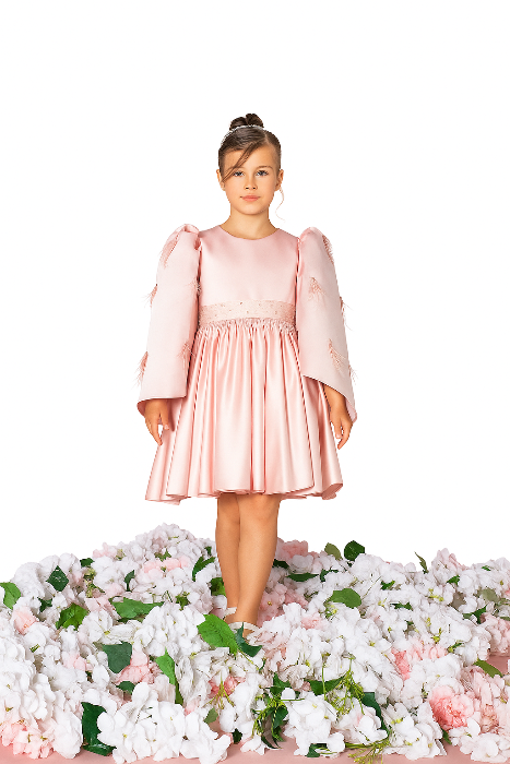 Young girl in a pink dress standing on a bed of flowers with a white background