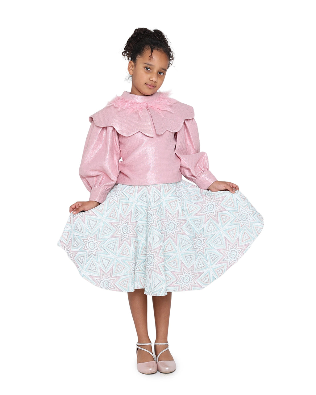 Young girl wearing a pink blouse with ruffled collar and a white skirt with blue patterns on a white background