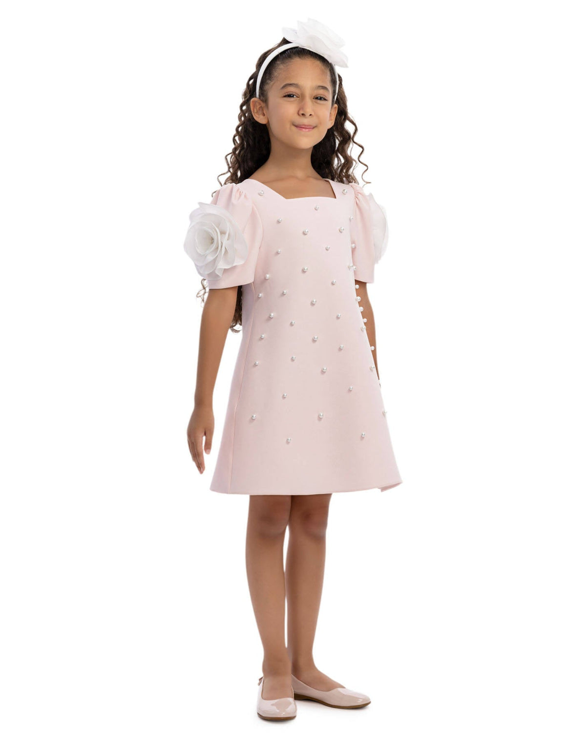 Young girl wearing a light pink dress with white flowers on a white background