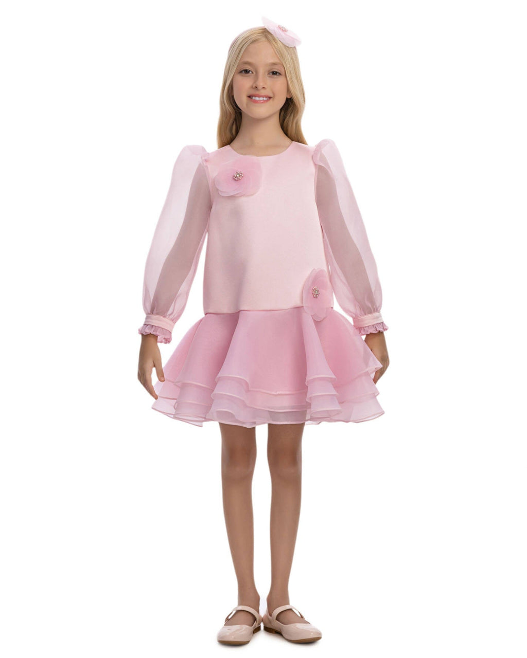Young girl wearing a pink dress with sheer sleeves on a white background